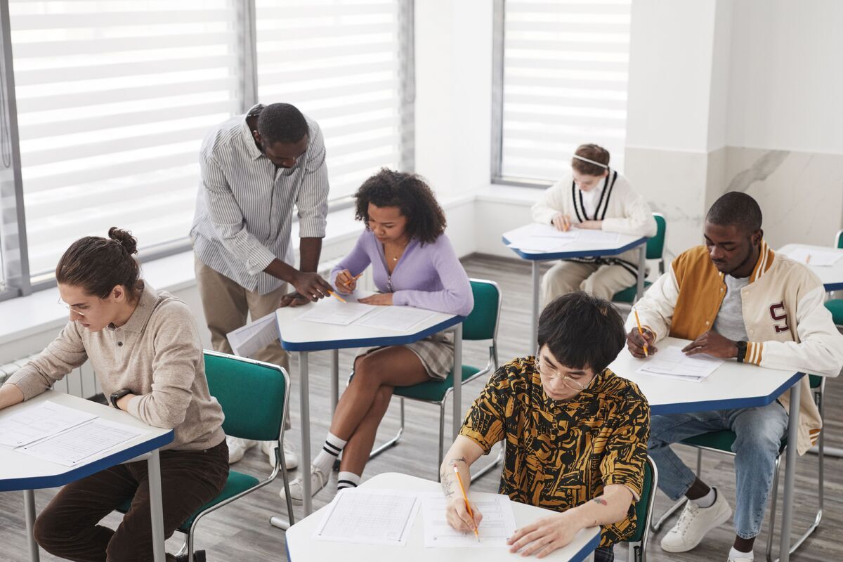Students completing a written assessment in a classroom while a teacher supervises.