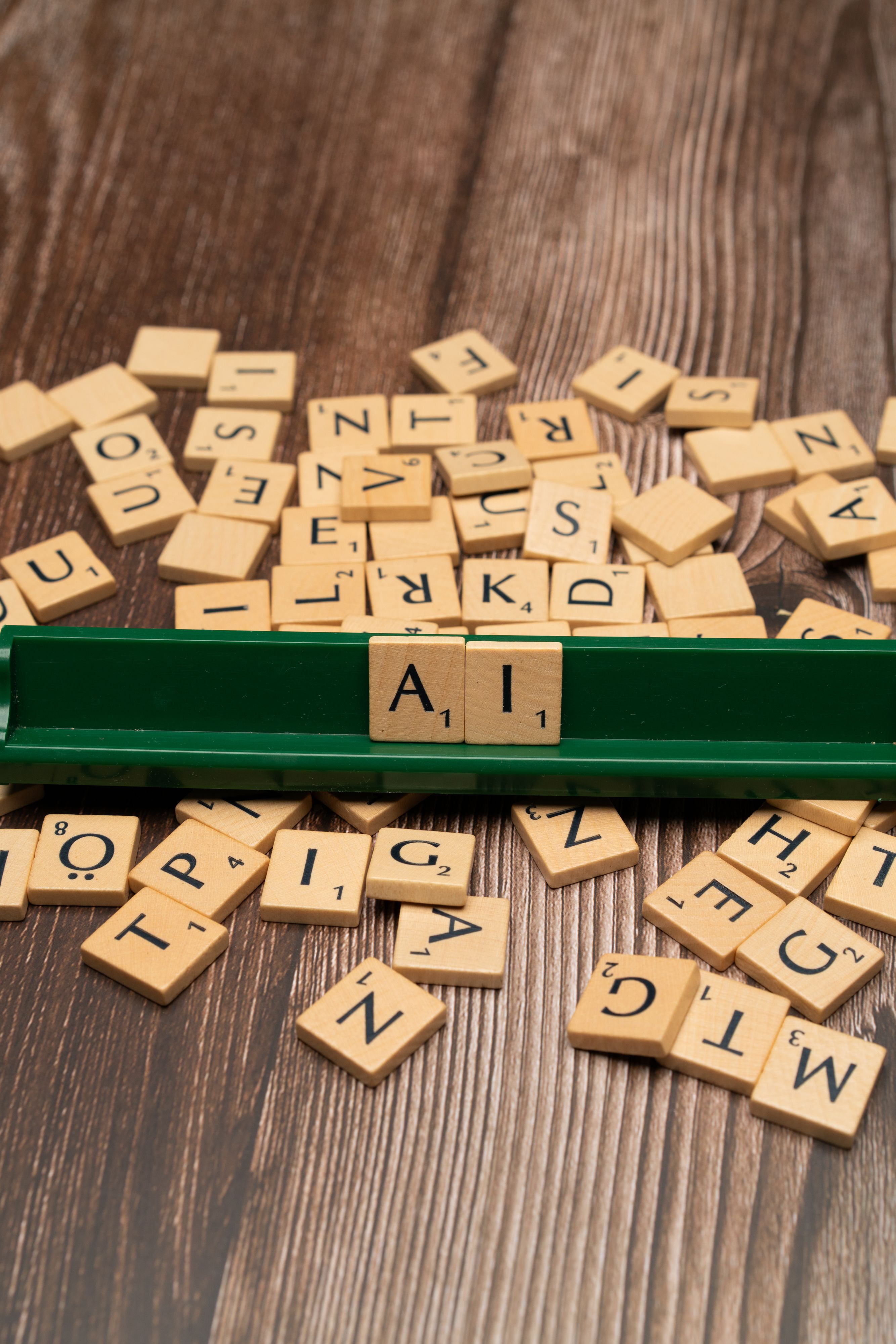 Wooden letter tiles spelling AI on a green rack, surrounded by scattered letters.